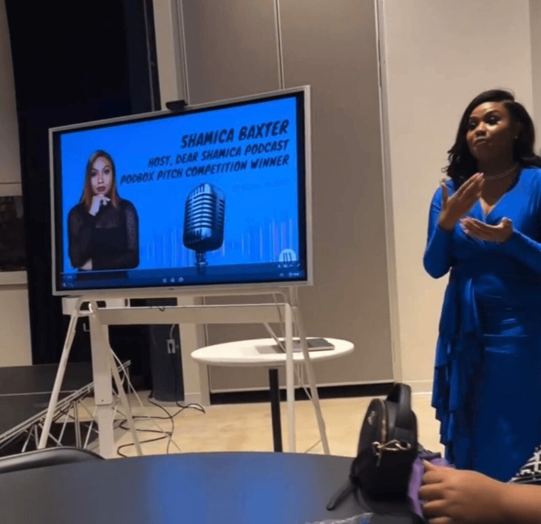 Shamica hosting an event beside a screen showing her name