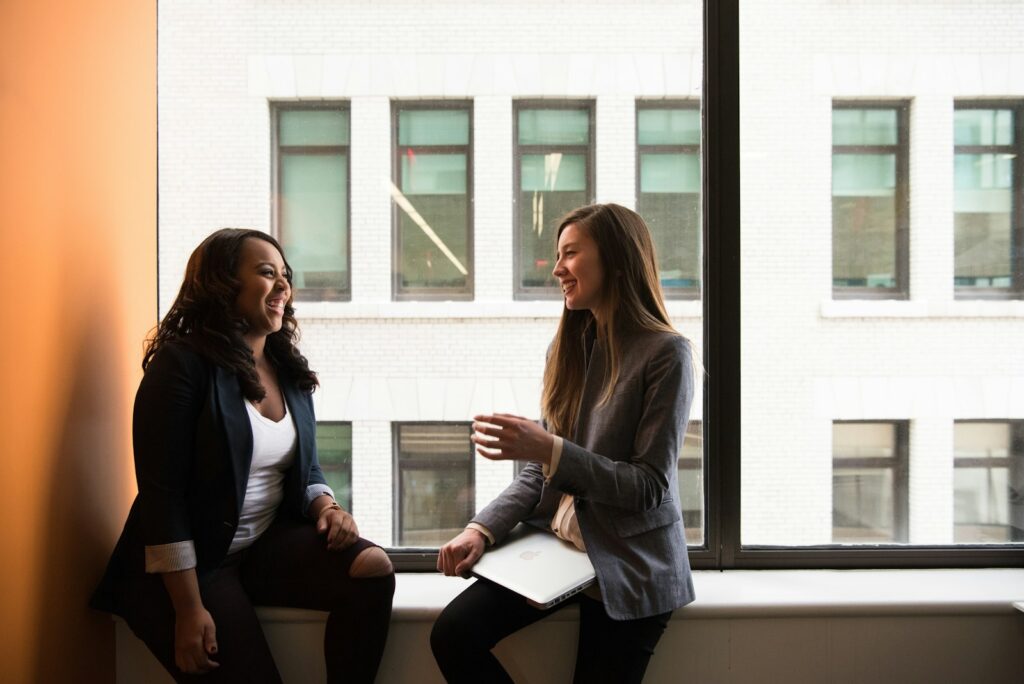 Two women laughing together by a sunny window